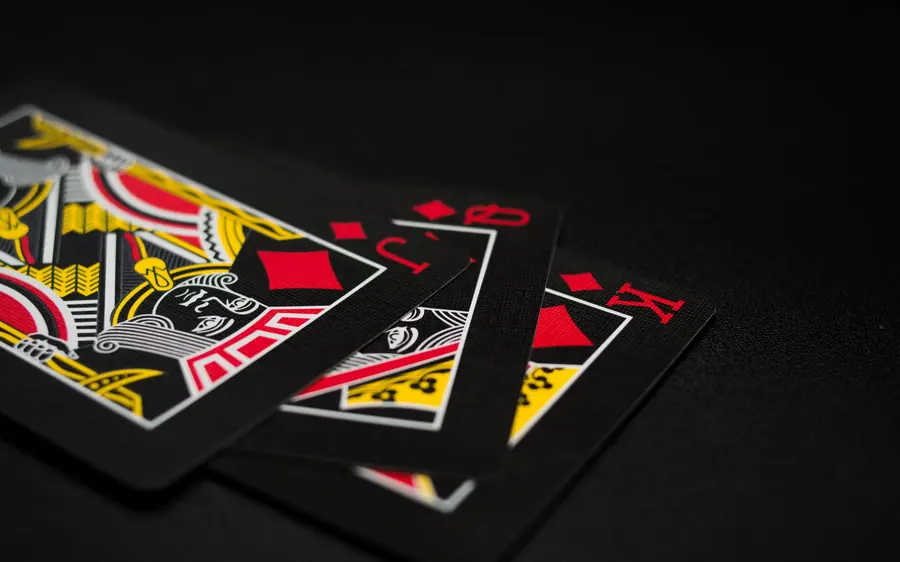 Three playing cards fanned on a black surface — a king, a jack and a second king, printed in red and gold on black backs