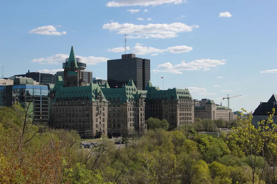 Ottawa’s downtown ridge in late spring, green copper roofs above bare and budding trees, a construction crane on the skyline