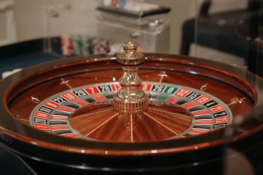 Close-up of a polished wooden roulette wheel with its brass centre spindle, red, black and green pockets in soft focus